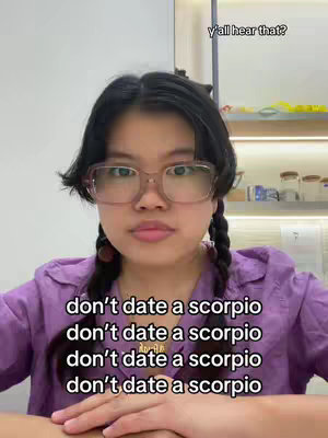 The cover image features a young woman with dark hair styled in braids. She wears glasses and a purple top. Text overlays repeat the phrase "don't date a scorpio". The background is a neutral, almost white wall. Above the woman's head, the phrase "y'all hear that?" appears. The composition is a medium shot, focusing on the upper body and face.