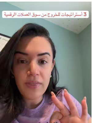 A woman is filming herself in what appears to be an indoor setting, likely a home office or workspace. A sign in the upper left corner is slightly visible. The woman is centered in the frame as she makes the Ok gesture, with her fingers in a circle.