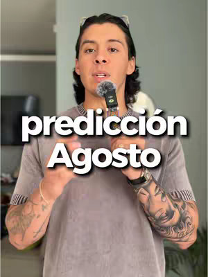 A medium shot of a man holding a microphone, with the overlay text 'prediccion Agosto' in a large, white, bold font. The man has short, dark hair and is wearing a grey t-shirt. Tattoos are visible on his arm. The background seems to be a home interior with a grey wall.