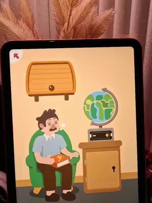 An iPad screen displaying an illustrated scene from what appears to be a puzzle game. A cartoon man is seated in a green armchair, holding a book with a lightning bolt on it. Behind him, on the screen, is a wooden chest attached to the wall. To his right is a table holding a globe and small cabinet. The background is a peach color. The screen is held in a border of an electronic device and in the back, some dried flowers is visible