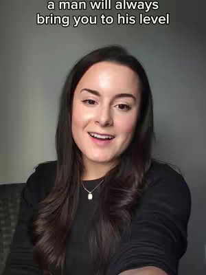 A woman with long dark hair and a black top is looking at the camera and smiling. The background is a plain grey wall. White text overlay at the top says 'a man will always bring you to his level'.