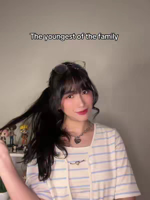 A young woman with long dark hair, wearing glasses on her head is featured. She has pink blush and red lipstick on. She wears a horizontally striped shirt and a small silver necklace. The background is a light solid color.