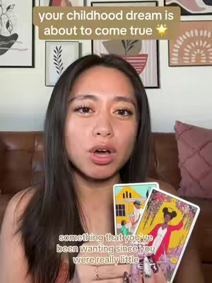 A woman is centered in the frame, holding tarot cards. The background features framed artwork and a soft, warm-toned color palette. Text overlays appear in the top and bottom of the frame.