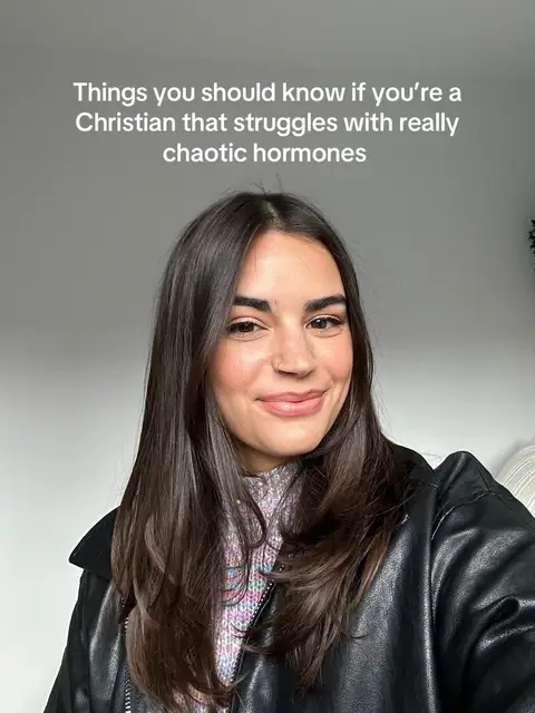 A woman with long, dark hair is smiling at the camera. The image is a selfie, with text added at the top. She wears a black leather jacket over a patterned top.