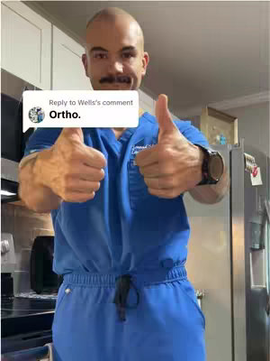 A man with a bald head, dark mustache, and is wearing blue scrubs flashes a double thumbs-up gesture, with an overlay of a comment reply. The background hints at an indoor setting, with kitchen appliances subtly visible.