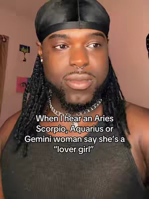 A selfie-style shot featuring a Black man with a durag, nose ring, and chain necklace. The text overlay reads a phrase about zodiac signs and lover girls. The lighting is natural-looking, and the background is a soft, neutral color.