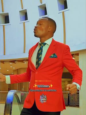 The cover image features a man in a red blazer, white shirt, and patterned tie, standing in front of a modern building. He is looking upwards with his mouth open, as if singing. Text overlays include a song title, artist names, and a logo.