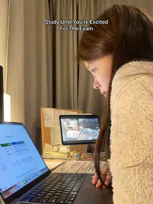 A woman studies in front of her laptop. The image is in focus on that subject and shows a warm, indoor setting with soft lighting.
