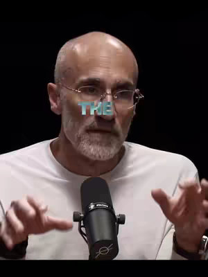 A man with glasses and a white shirt is speaking into a microphone. The word "THE" is superimposed in a text overlay on his face. The background is black.