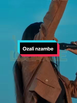 The cover image features a person, likely a woman, holding a microphone and singing. The background is a blurred teal color, and the person is wearing a brown jacket. Overlaid on the image is a rectangular box with the text 'Ozali nzambe'.