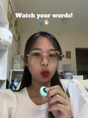 A young woman is centered in the frame, wearing glasses and appearing to be talking. The background is somewhat blurred, but shows a room with some decor. Text overlays the image.