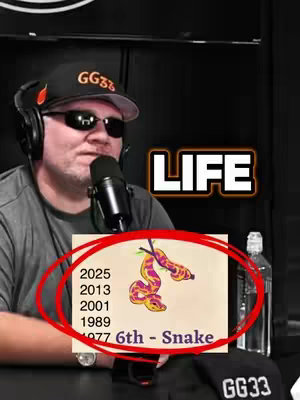 A man wearing a black cap and sunglasses is holding a microphone and presenting a screenshot with a red circle on it. The screenshot has an illustration of two snakes, the years 2025, 2013, 2001, 1989, and 1977, and text that reads '6th - Snake,' positioned under the snake image. The background appears dark, complemented by a bottle of water and a black cap branded with the letters 'GG33.' The word 'LIFE' appears in large white letters.