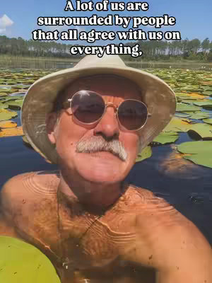 A middle-aged man wearing sunglasses and a sun hat is in a body of water filled with lily pads, appearing shirtless with water droplets on his skin, providing a close-up shot of his face and upper body.