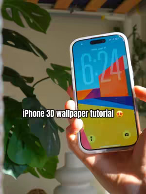 A hand holds an iPhone displaying a colorful 3D wallpaper, with plant leaves in the background. The phone is in the center, showcasing a design with blue, orange, and yellow segments and the time displayed. In the foreground, a hand holds the phone against a background of green leaves.