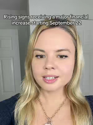 A close-up shot of a woman with blonde hair and a necklace, speaking directly to the camera. The background is a plain white wall with a white door. The overall composition is simple and focuses on the woman's face and upper body.