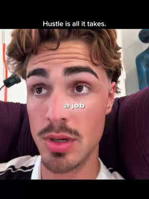 A close-up shot of a young man with brown hair and a mustache, looking directly at the camera. The overlay text displays the word 'a job.' The background includes a glimpse of a blue sculpture and a purple surface.