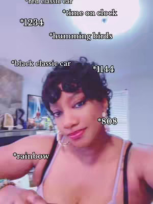 A woman with short dark hair is taking a selfie. She has fair skin, a small nose with a thin, somewhat smiling lips. She is wearing hoop earrings and a camisole top. Several text overlays float around her head, each with a star before the word: red classic car, time on clock, 1234, humming birds, black classic car, 1144, rainbow, and 808. The background is a room with windows and a view of a bright, sunlit sky.