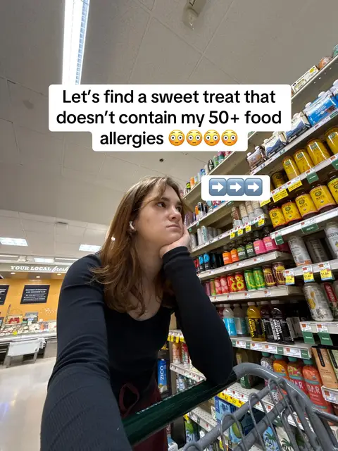 A young woman stands pensively near a grocery store aisle, her arm resting on an attached shopping cart. She has white earbuds in and looks upward, with a text overlay above. The shelves behind her are stocked with various products, creating a backdrop for her pose in a well-lit setting.