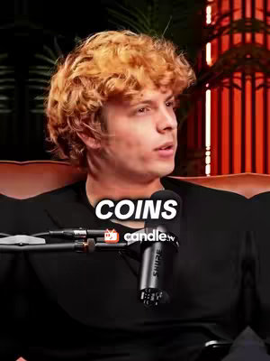 A man is seated on a couch, possibly in a studio setting. The background includes a dark area with a red striped structure. The man, with curly light-brown hair, is looking slightly off-camera. A superimposed text overlay reads "COINS", along with logos for a relevant app.