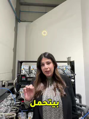 A woman is standing in front of a server rack in a well-lit room. She is wearing a blazer and a patterned top. The background appears to be a technical space, with white walls, and piping near the ceiling. Text in Arabic is overlaid on the image.