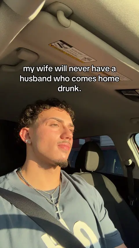 A young man is seated inside a car, angled slightly to the side, with the sunlight hitting his face. He is wearing a grey t-shirt. Text overlay is present at the top of the image. The car's interior is visible, with the ceiling and part of the driver's seat in view.