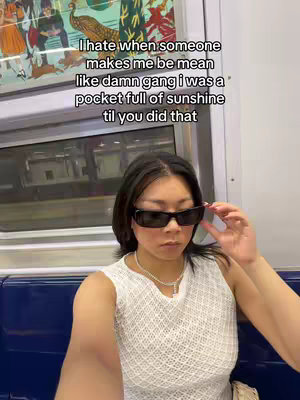 A selfie-style shot inside a train car. A person of Asian descent is the primary focus. They are wearing sunglasses and a white, textured top. The background includes train windows and seating. Added text overlay is visible in the top of the frame.