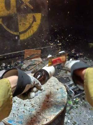 A first-person perspective shows gloved hands swinging and smashing a wine bottle against a surface, causing it to break. The background includes graffiti and debris.
