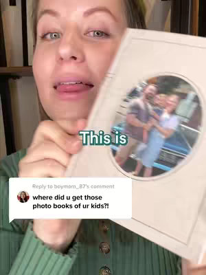 A woman is shown holding a photo book in front of her. The woman has a friendly expression. The book is open, revealing a photograph. The background is blurred.