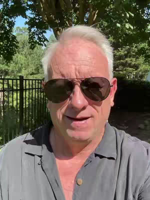 The cover image features a mature man, facing the camera in a medium shot. He wears a grey button-down shirt and dark aviator sunglasses. His short, graying hair is neatly styled. The backdrop includes a green, leafy environment with a fence visible on the left and the sun is shining. The composition has a natural, outdoor setting.