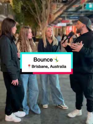 A group of four people is gathered outdoors, likely in a city setting. A man holding a microphone is interviewing three other individuals: two women and one other person. A text overlay shows the word "Bounce" and the location: Brisbane, Australia.