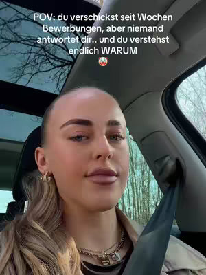 A selfie-style shot with a woman in the driver's seat of a car. Text overlays the top part of the image. The woman has blonde hair pulled back from her face. She is wearing a light-colored jacket and multiple necklaces. The background shows the car's interior and an outside view.