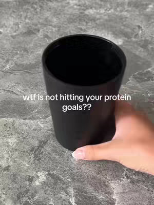 A close-up of a hand holding a black, cylindrical cup, with a grey speckled surface beneath. White text is overlaid on the image.