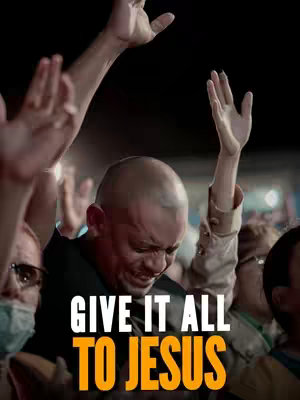 A vertical shot of a group of people with their hands raised in the air, with a central figure in the foreground, eyes closed and hands up, with the text "GIVE IT ALL TO JESUS" overlaid in large, bold, yellow-outlined white letters.