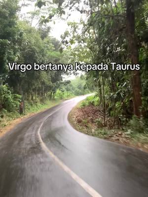 The cover image shows a winding road through a lush, green forest. The road is wet, suggesting it has recently rained. Text overlayed on the image reads, 'Virgo bertanya kepada Taurus'. The scene is captured in a vertical format.