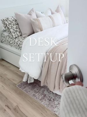 The cover image shows a bedroom scene with a large bed as the central focus. The bed is neatly made with white bedding and numerous pillows. A soft pink knitted blanket adds a touch of color. The words 'DESK SETUP' are overlaid on the image in a white font. A door and a hand holding the doorknob occupy the right edge, suggesting an entry point or transition.
