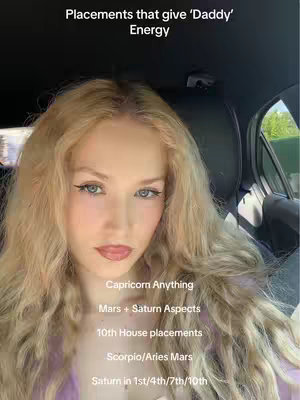 A selfie-style image featuring a woman sitting in a car. She has long blonde hair and fair skin, and she is looking at the camera. Above her in text, it says 'Placements that give Daddy Energy' then lists several astrological signs below. The overall composition emphasizes personal presentation within a casual environment.