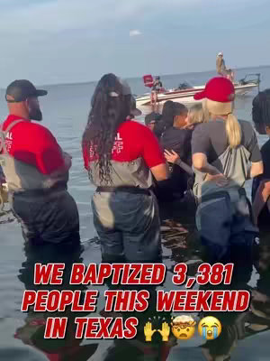 The image shows a group of people standing in shallow water, appearing to be a baptism. Several individuals are partially submerged, with others standing nearby. A boat is visible in the background. Overlay text states the number of baptisms and location.
