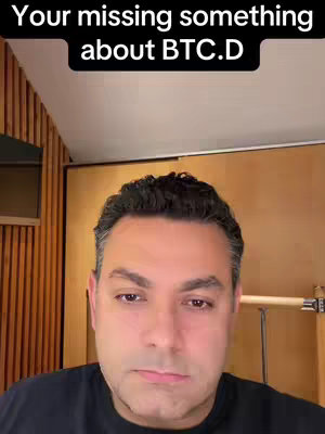 A man with dark hair is centered in a video frame, with a black bar at the top of the screen containing white text. The background includes light-colored wooden panels and a door.