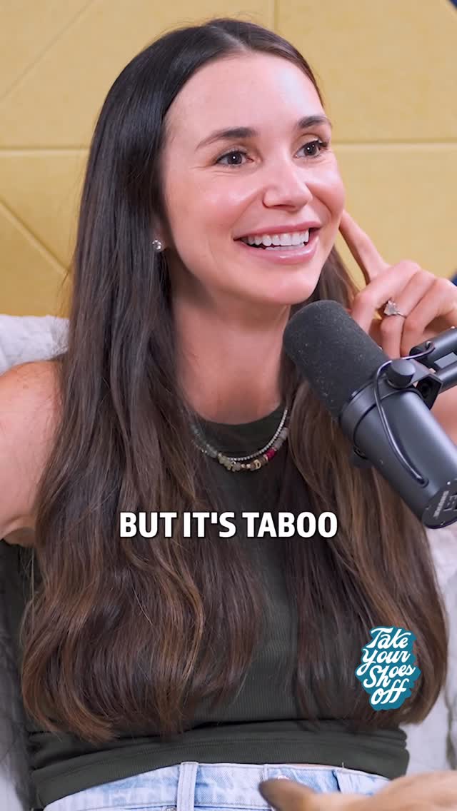 A woman with long, dark hair smiles and gestures while holding a microphone in front of her. She is wearing a green top. Text overlay reads "BUT IT'S TABOO". She is also wearing a necklace, earrings and a ring.