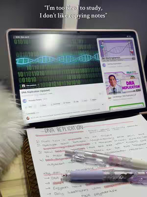 A close-up shot of a desk with open notebook and pens. A laptop displaying information about DNA replication and a cell biology video are positioned in the backdrop. The notebook is filled with handwritten notes, with pens casually placed on top. The overall composition suggests a study or learning environment, with soft, diffused lighting.