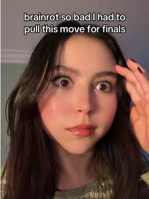 A close-up shot of a young woman with dark hair and fair skin. She has wide, startled eyes and is holding her hand up to her forehead with a look of shock or surprise. The background is slightly blurred.