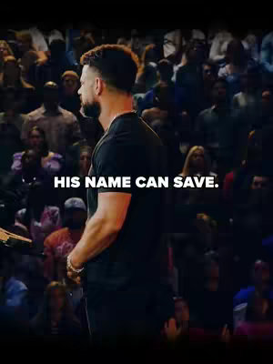 A man from the back is standing in front of a large audience. The man is facing away from the camera, and has short, dark hair and is wearing a black t-shirt. The words "HIS NAME CAN SAVE." are in white text overlayed in the middle of the screen.