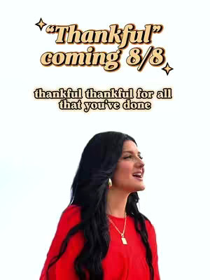 A woman with long black hair in a red top looks up to the right with a smile. Text overlays in a fancy font announce the song "Thankful" coming on 8/8, another text reads "thankful thankful for all that you've done".