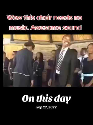 The image shows a choir performance. The foreground features a man in a suit smiling and looking at others, with the choir members in the background. Text at the top reads, "Wow this choir needs no music. Awesome sound."