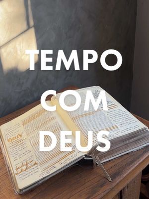 An open book with handwritten notes and a bookmark sits on a wooden surface; overlayed in white block letters is the text 'TEMPO COM DEUS'. The background is a gray wall with a shadow from a window.