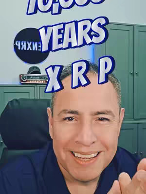 A selfie-style video cover featuring a man smiling, with text overlays related to XRP cryptocurrency. The man has short hair and is wearing a dark blue collared shirt. The background shows a home office setting. Text elements include the phrase '10,000 YEARS' above and 'XRP' at the top of the man's head.