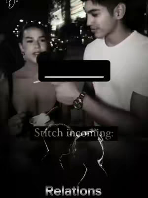 A black and white photo shows a man and a woman. The woman is on the left side of the image, and the man is on the right. The woman is looking up and to the right, away from the camera. The man is looking towards the woman and pointing something at her.