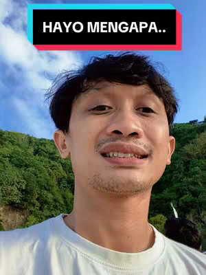 A man with a mustache smiles at the camera against a blurred background of green foliage and a blue sky. A rectangular black and red text box is overlaid at the top of the image.