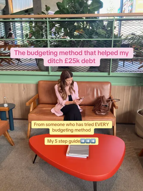 A woman sits indoors on a brown leather couch, holding a phone. A red coffee table in front holds a book. Text overlays highlight the topic: a budgeting method that helped her pay off debt. The background includes a green trellis.