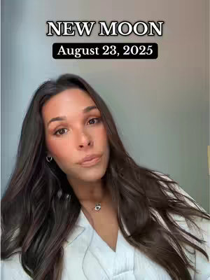 A woman with long, wavy dark hair, wearing a white top and a necklace, looks up at the camera. The image has a backdrop that is slightly grey. Text at the top says 'NEW MOON' and underneath this, the date 'August 23, 2025' in a black rectangle.